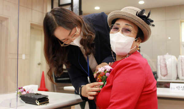 어르신에게 꽃을 달아드리는 문촌9종합사회복지관 관계자.