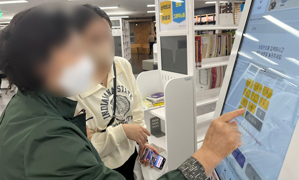  어르신이 도서관에서 무인대출기를 사용하고 있다.