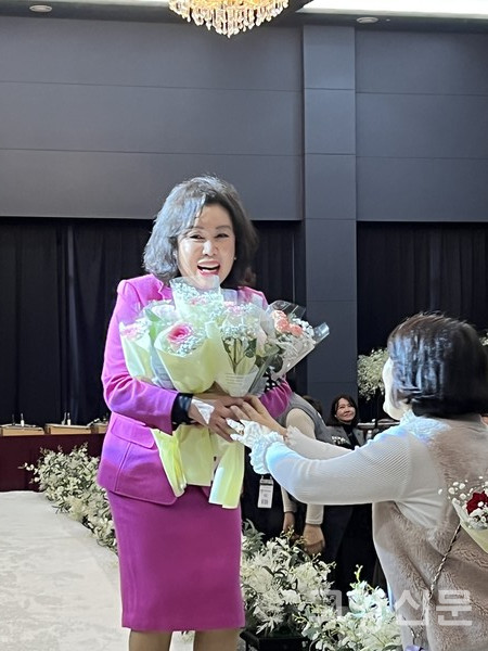 동문들이 준비한 축하 꽃다발을 가득 안고 무대로 오르고 있는 박미화 신임 회장.