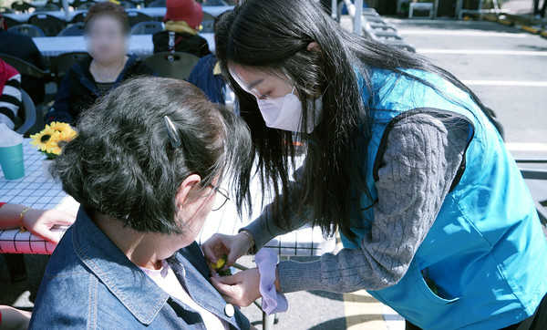 복지관의 한 관계자가 어르신에게 꽃을 달아드리고 있다.