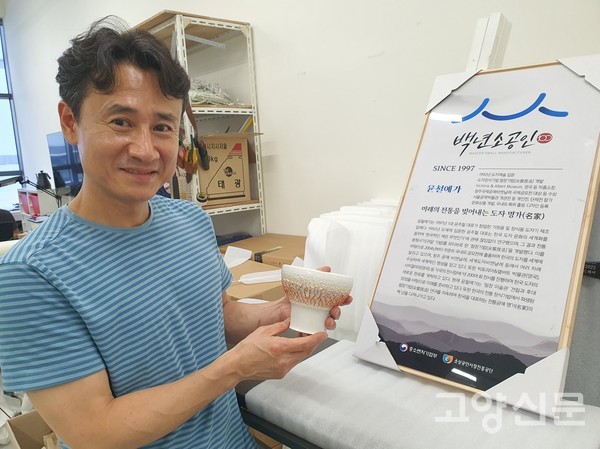 윤주철 대표가 백년소공인 표지판 앞에서 첨장기법 작품을 보여주고 있다.