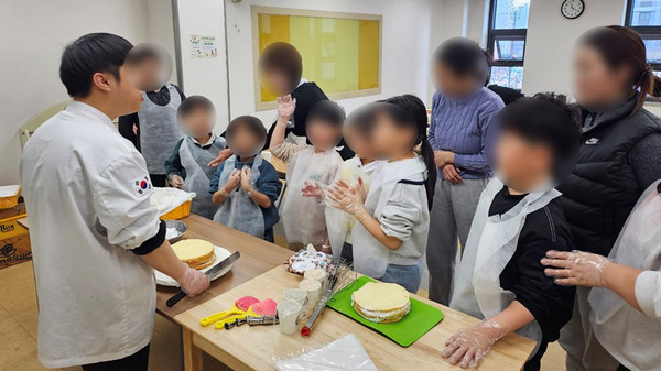 참여자와 참여자의 부모들이 모여 케이크를 만드는 과정에 대한 설명을 듣고 있다.