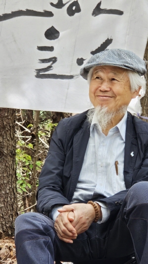 23일 ‘『초록법설』의 봄’ 행사에서 700여 년 세월의 나이테를 품고 있는 산황동 용뿔 느티나무 아래에 앉아있는 홍일선 시인. [사진=최윤정]