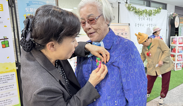 심재경 흰돌종합사회복지관장이 어르신에게 카네이션을 달아드리고 있다.