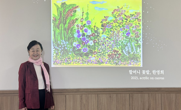  한영희 작가가 '할머니 꽃밭'의 작품 앞에서 환하게 웃고 있다.