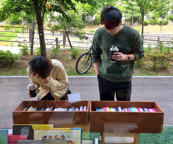 천변을 산책하는 주민들이 '미스터 버티고' 책방 앞을 들러 가판대의 책을 살펴보고 있다. 