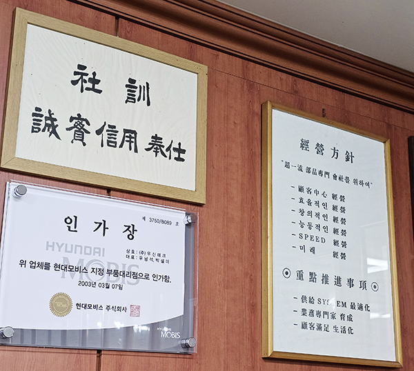 우신테크 사무실 벽에 나란히 걸려있는 사훈과 현대모비스 지정 부품 대리점 인가장, 긔리고 경영방침.