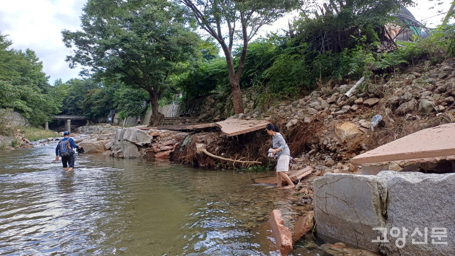 솔내음누리길을 걷던 주민들이 산책로가 파손된 구간을 지나가기 위해 신발을 벗고 물속으로 들어가고 있다. 