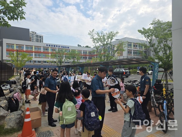 "안전한 학교 만들어요". 고양경찰서 소속 경찰관이 등교하는 지효초등학교 학생에게 학교폭력 예방 문구가 인쇄된 캐릭터 부채를 전달하며 인사를 나누고 있다.