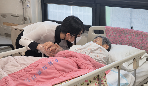 대학생 서포터즈가 병실에서 어르신의 손을 잡고 이야기를 나누고 있다. 